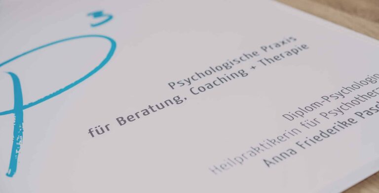 Nahaufnahme eines Dokuments mit deutschem Text und einem stilisierten blauen „P“. Im Text finden sich Formulierungen wie „Psychologische Praxis“, „für Beratung, Coaching + Therapie“, „Diplom-Psychologin“, „Heilpraktikerin für Psychotherapie“ und „Anna Friederike Paulsen“. Experte Printdesign Aachen.