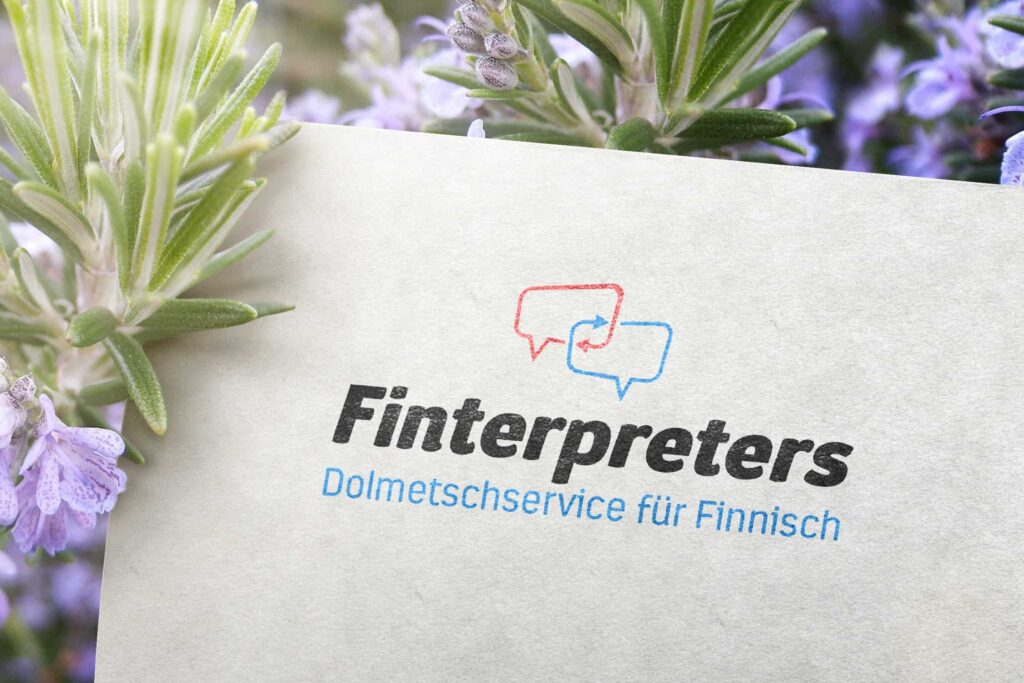 Ein weißes Blatt Papier mit dem Logo von „Finterpreters“ und dem Text „Dolmetschservice für Finnisch“ ist von blühenden Lavendelblüten umgeben. Das unseren Kunden aus Aachen bekannte Logo zeigt zwei Sprechblasen in Rot und Blau mit einem Handschlag darin.