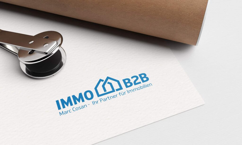 Ein Papier mit einem blauen Logo aus zwei sich überlappenden Häusern neben dem Text „IMMO B2B“ und „Marc Cosan – Ihr Partner für Immobilien“ darauf gedruckt. Das Papier, teilweise bedeckt von einem braunen gerollten Dokument, das von einer Metallklammer gehalten wird, unterstreicht die Exzellenz von Webdesign Aachen.