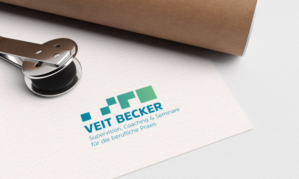 Ein Zettel mit dem Logo und dem Text „Veit Becker, Supervision, Coaching u0026 Seminare für die berufliche Praxis“ in Blau und Grün. Auf dem Zettel liegt ein Locher, daneben liegt auf einer weißen Fläche ein zusammengerolltes braunes Papier.