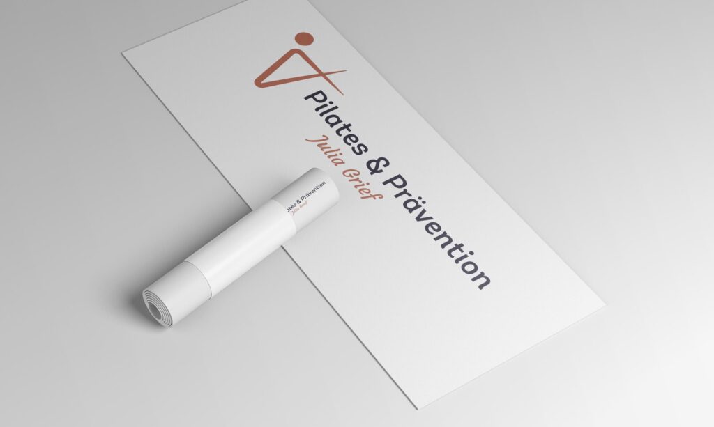Eine weiße Yogamatte mit dem Aufdruck „Pilates u0026 Prävention Julia Grief“ und einem minimalistischen Logo in Form einer menschlichen Figur liegt teilweise ausgerollt auf einem hellen Untergrund.